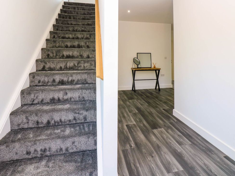 A hallway with stairs and a table with a mirror at Silver Birch Cottage in Frizington
