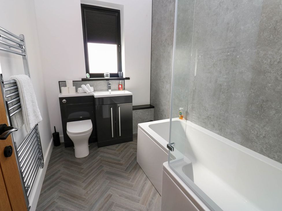 A bathroom featuring a bath tub, toilet, and sink at Silver Birch Cottage in Frizington