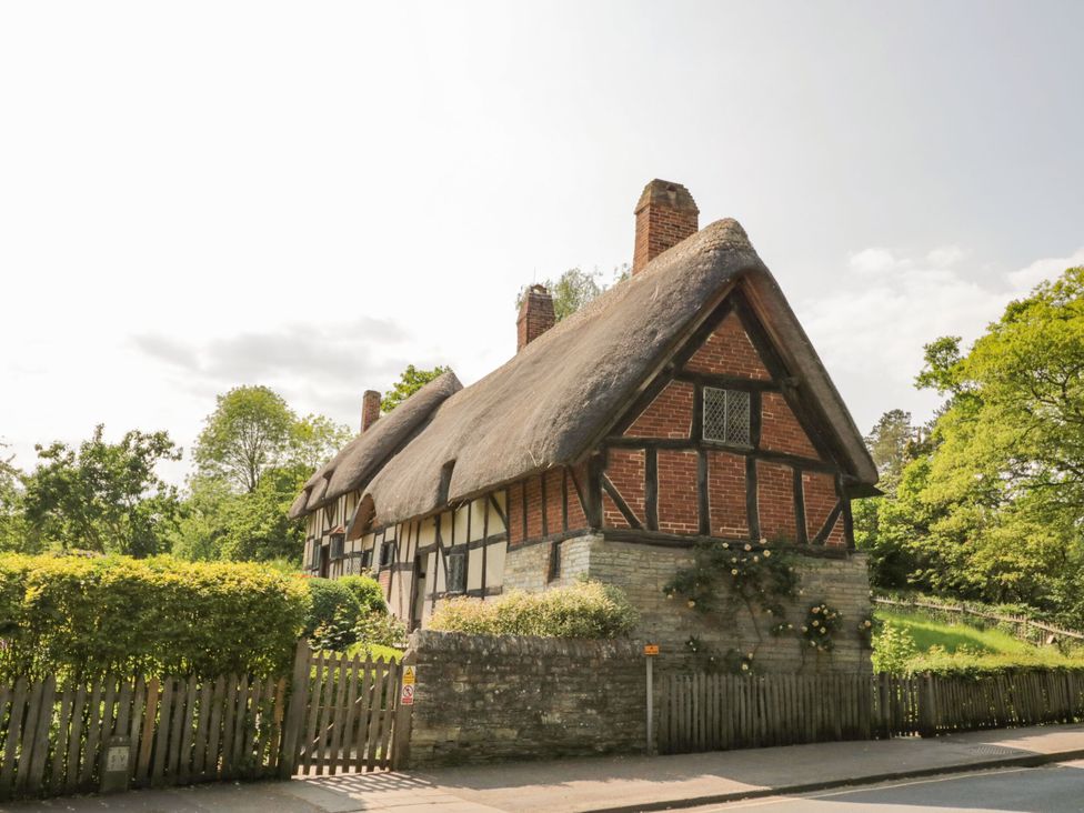 A thatched house with a wooden fence and garden at Albert Cottage Stratford-upon-Avon