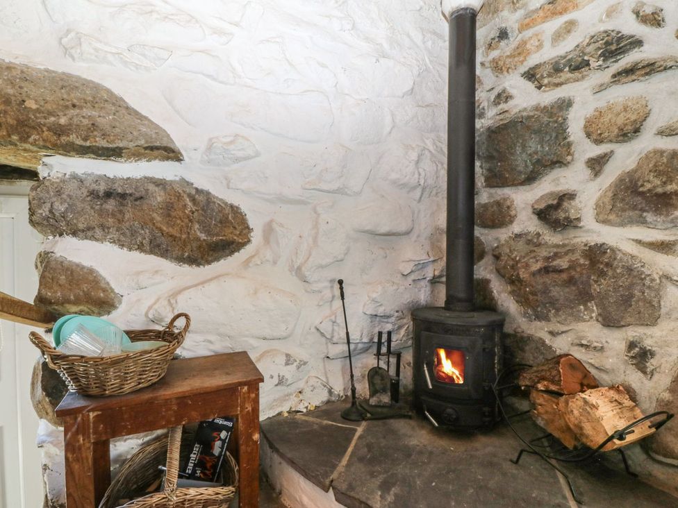 A living room with a wood stove and stone wall at Ty Coch in Caernarfon
