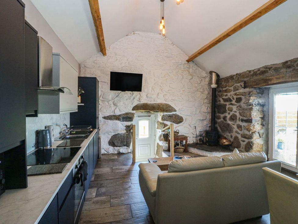 A living room with a kitchen area and a stove at Ty Coch in Caernarfon