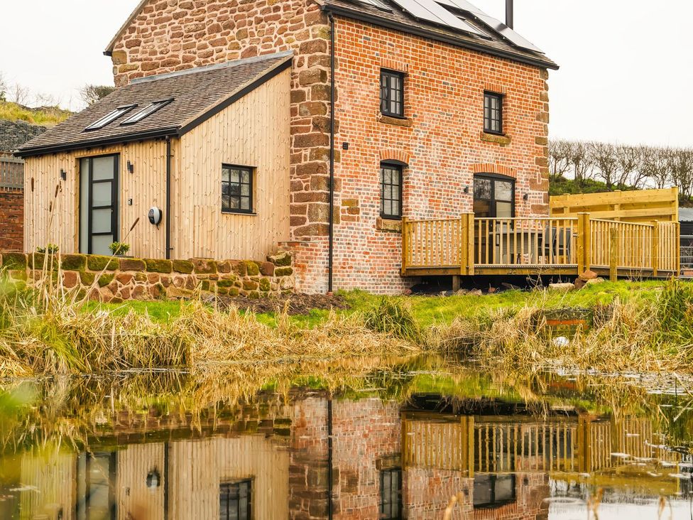 A house with a wooden deck by a body of water at The Old Mill in Great Bolas near Telford
