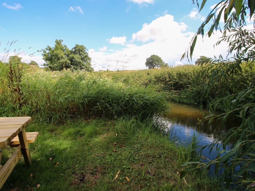 A view of grass and water with a bench at The Old Mill in Great Bolas near Telford