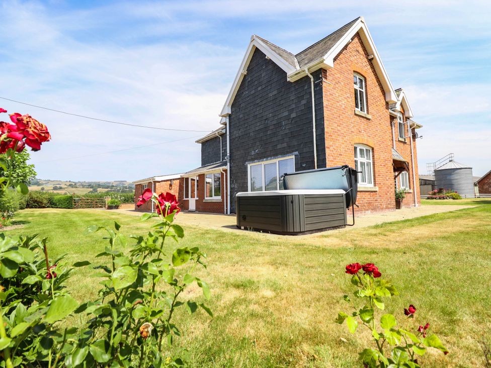 A house with a hot tub and roses in the garden at Pwll Glas Caersws