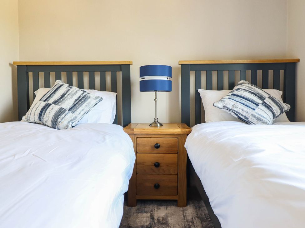 A bedroom with two beds and a bedside table at Pwll Glas in Caersws