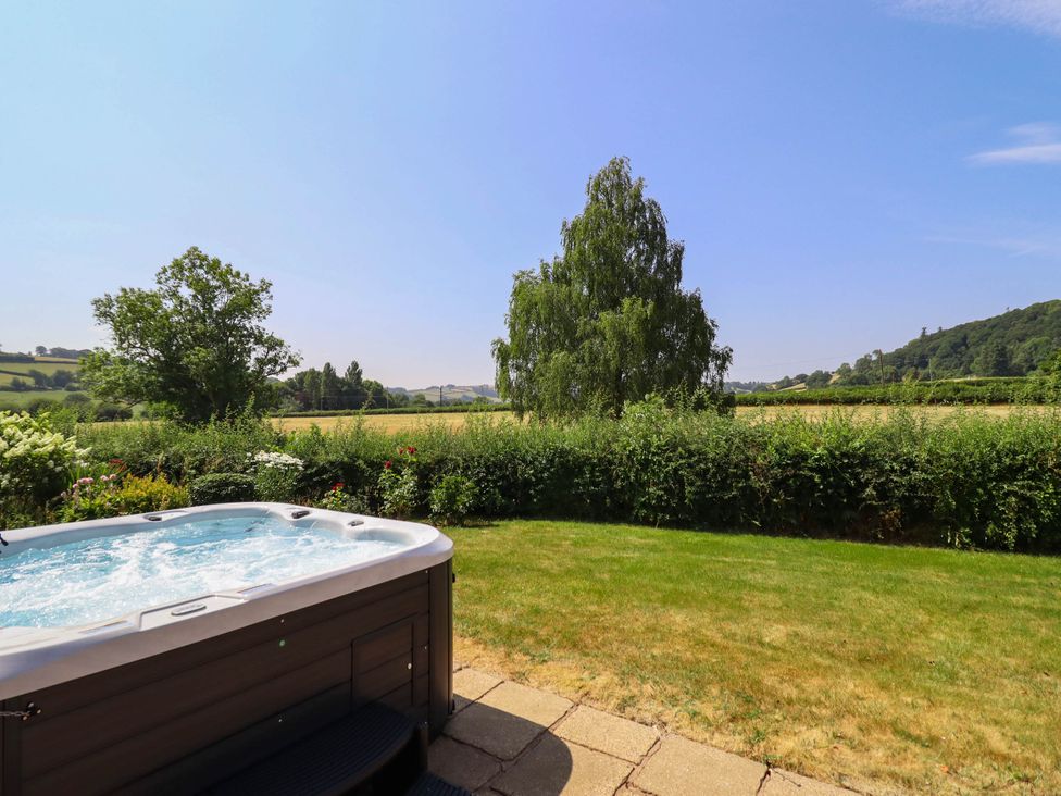 A hot tub in a garden with a view of fields and trees at Pwll Glas in Caersws