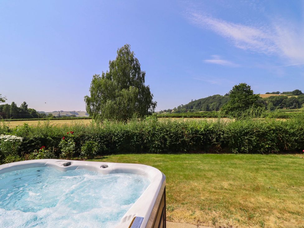 A garden with a hot tub and view of fields and trees at Pwll Glas in Caersws