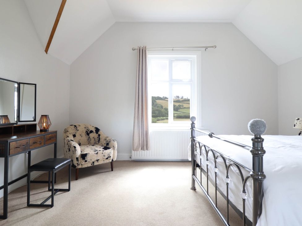 A bedroom with a bed, chair, and dressing table at Pwll Glas in Trefeglwys