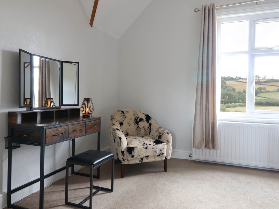 A bedroom with a vanity table and armchair at Pwll Glas Trefeglwys