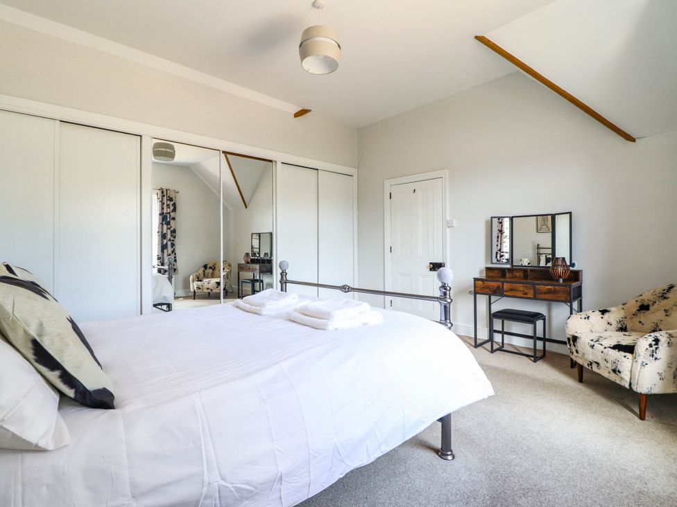 A bedroom with a bed, mirror, table and chair at Pwll Glas Trefeglwys