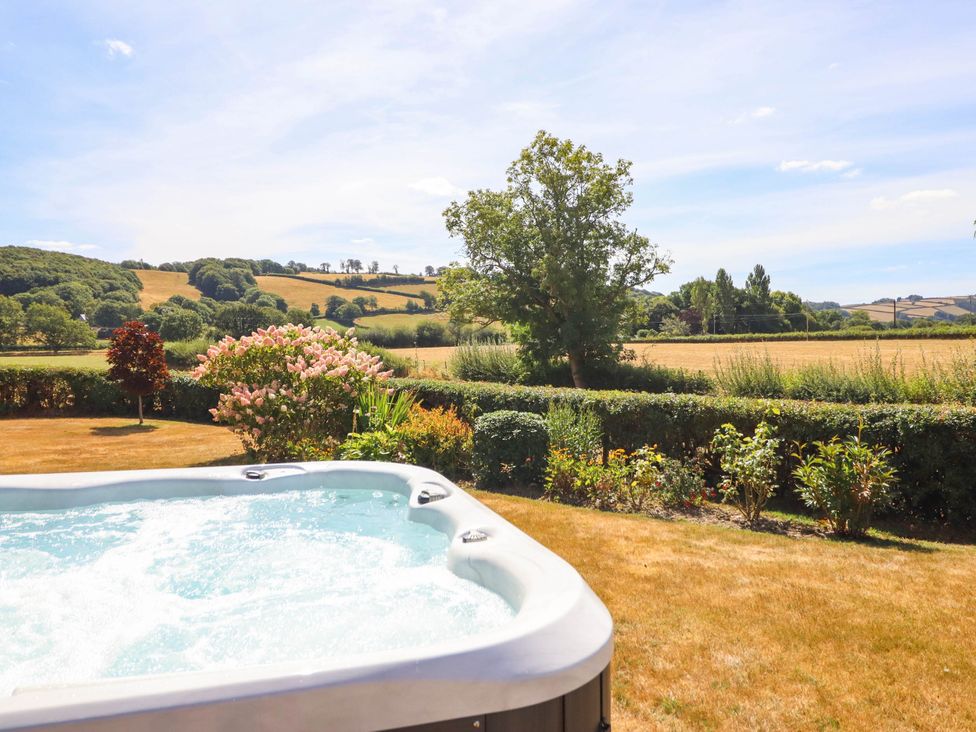 A hot tub in a garden with hills in the background at Pwll Glas Trefeglwys