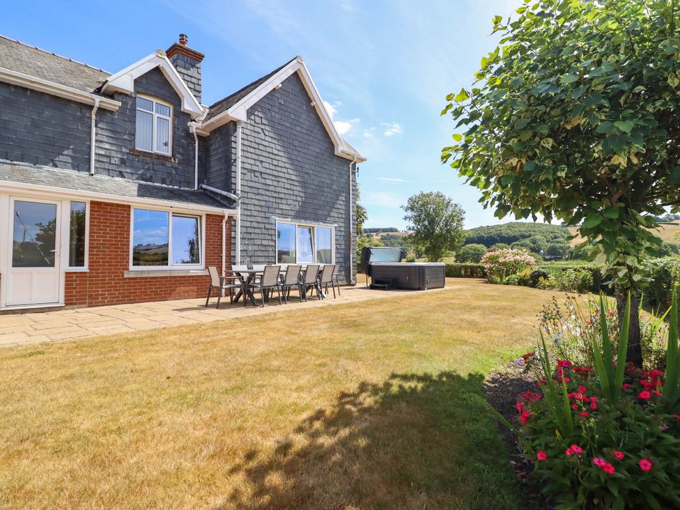 A garden with a patio, table, chairs, and hot tub at Pwll Glas, Trefeglwys