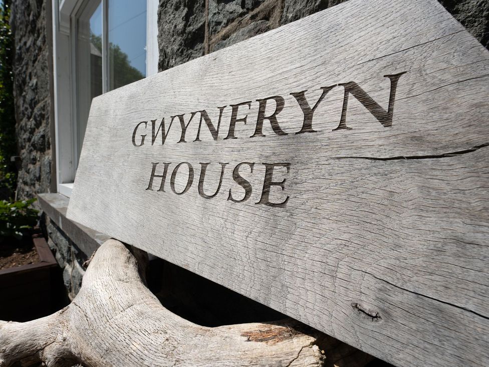 A wooden sign displaying Gwynfryn House outside a stone wall in Llanbedr