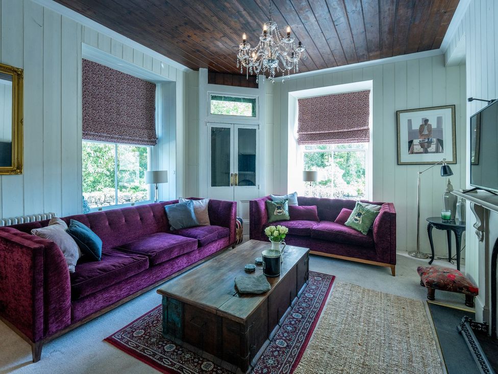 A living room with purple sofas and a wooden coffee table at Gwynfryn House in Llanbedr