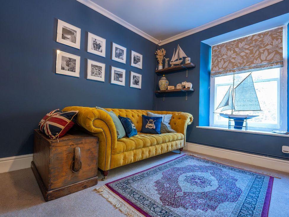 A living room with a yellow sofa and framed pictures at Gwynfryn House Llanbedr