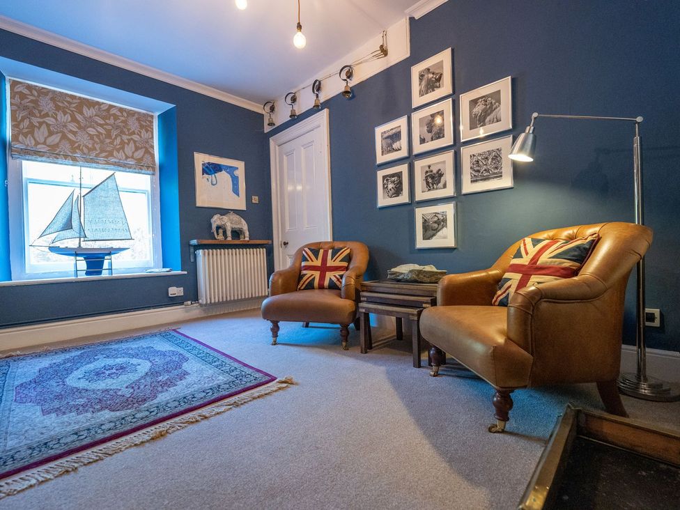 A living room with armchairs and a sailboat model at Gwynfryn House in Llanbedr