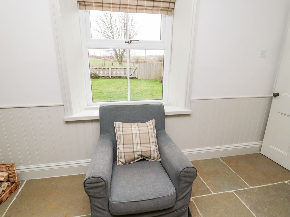 A sitting room with an armchair and a window at Canny Cottage in Belford
