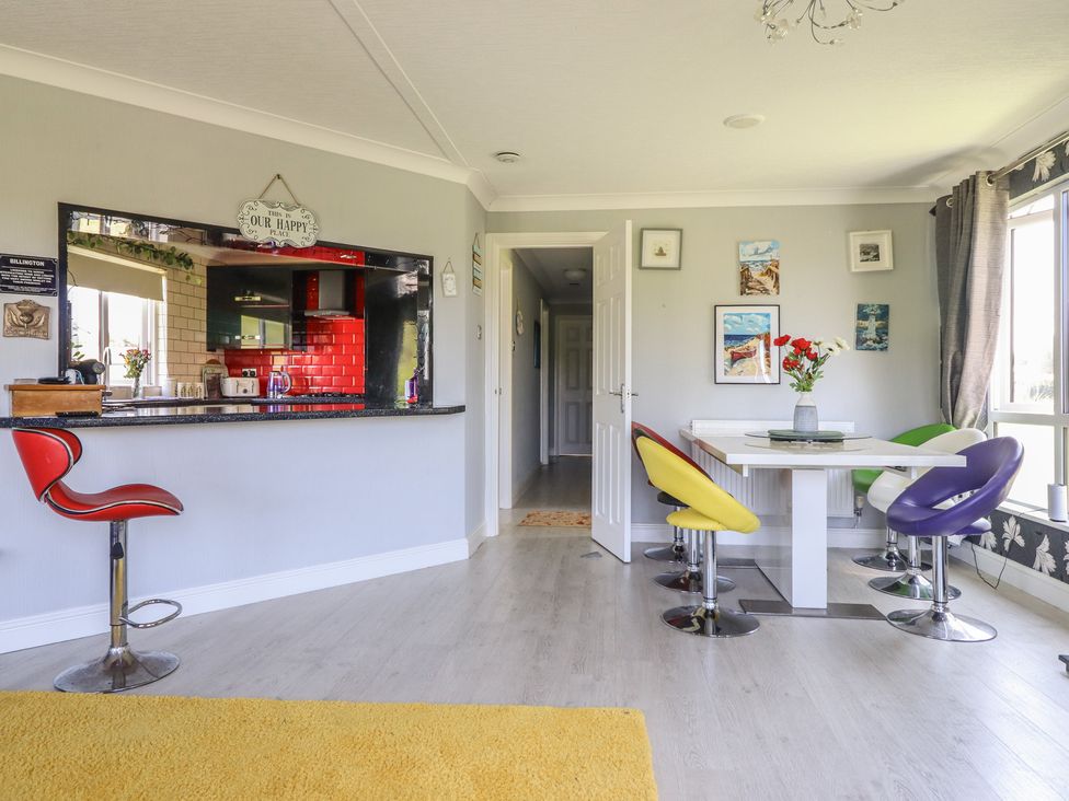 A dining room with a bar counter and colorful chairs at Excalabur 10 in Morfa Bychan
