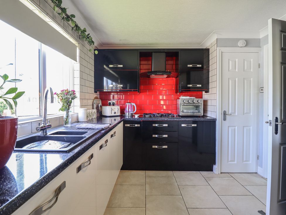 A kitchen with black units and red tiles at Excalabur 10 in Morfa Bychan