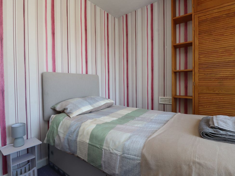 A bedroom with a bed, nightstand, and wardrobe at 31 Ffordd Y Maer in Pwllheli
