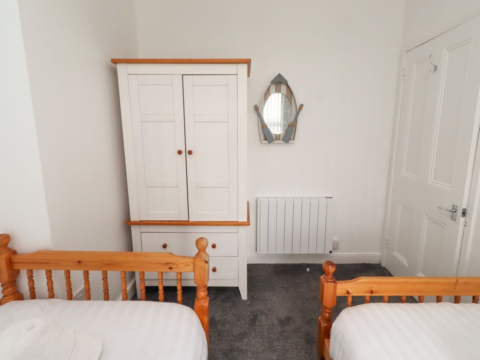 A bedroom with a wardrobe, two beds, and a mirror at 19 Dunstan View, Seahouses