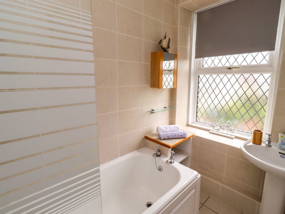 A bathroom with a bathtub, sink and window at 19 Dunstan View Seahouses