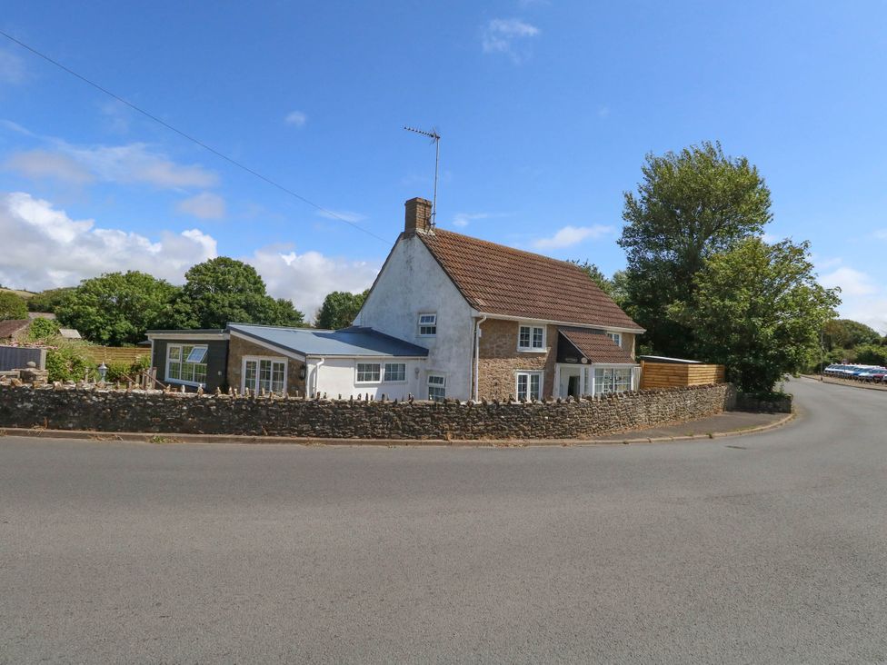 A house with a fence and trees beside the road at Greenwich Cottage in Burton Bradstock
