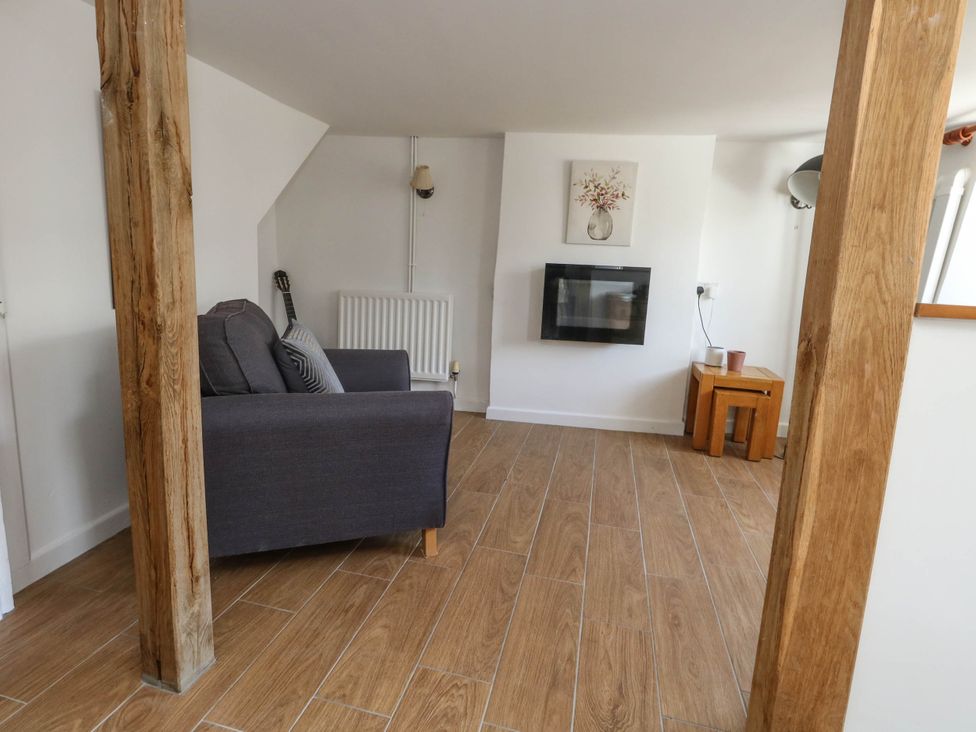 A living room with a sofa and electric fireplace at Greenwich Cottage in Burton Bradstock
