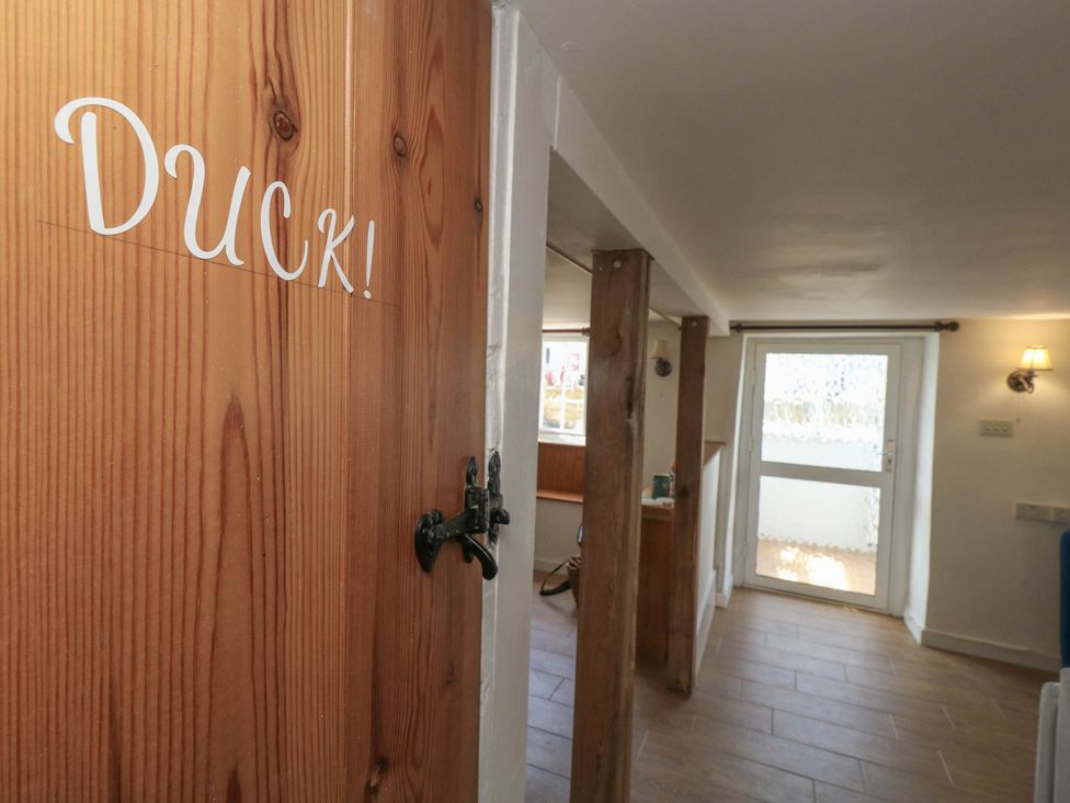 A hallway with a wooden door labeled Duck and a window at Greenwich Cottage in Burton Bradstock