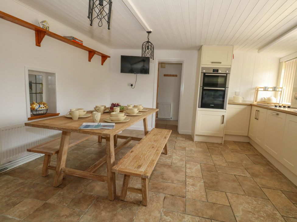 A dining room with a large table, benches and kitchen appliances at Greenwich Cottage in Burton Bradstock