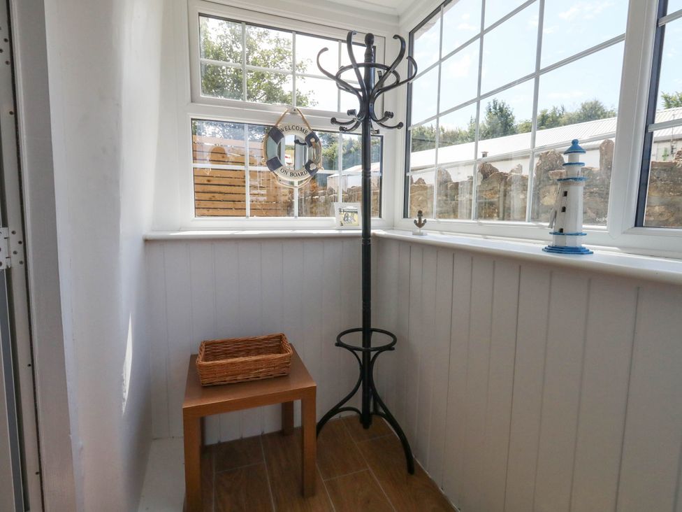 A conservatory with a coat rack and a table at Greenwich Cottage in Burton Bradstock