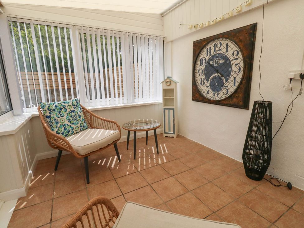 A conservatory with a clock and seating at Greenwich Cottage in Burton Bradstock