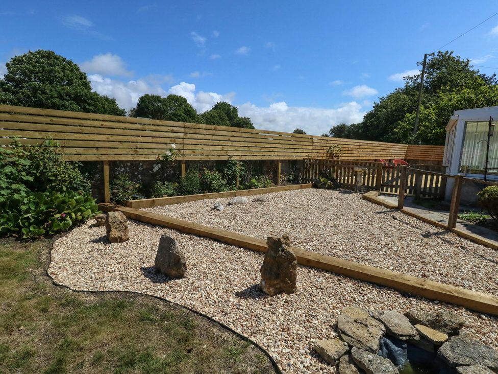 A garden with gravel, wooden fence, rocks and plants at Greenwich Cottage in Burton Bradstock