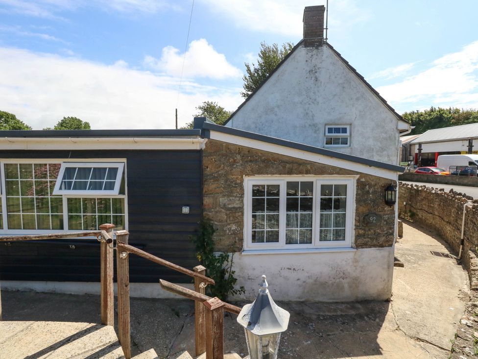 The exterior of a house with a stone wall and windows at Greenwich Cottage in Burton Bradstock
