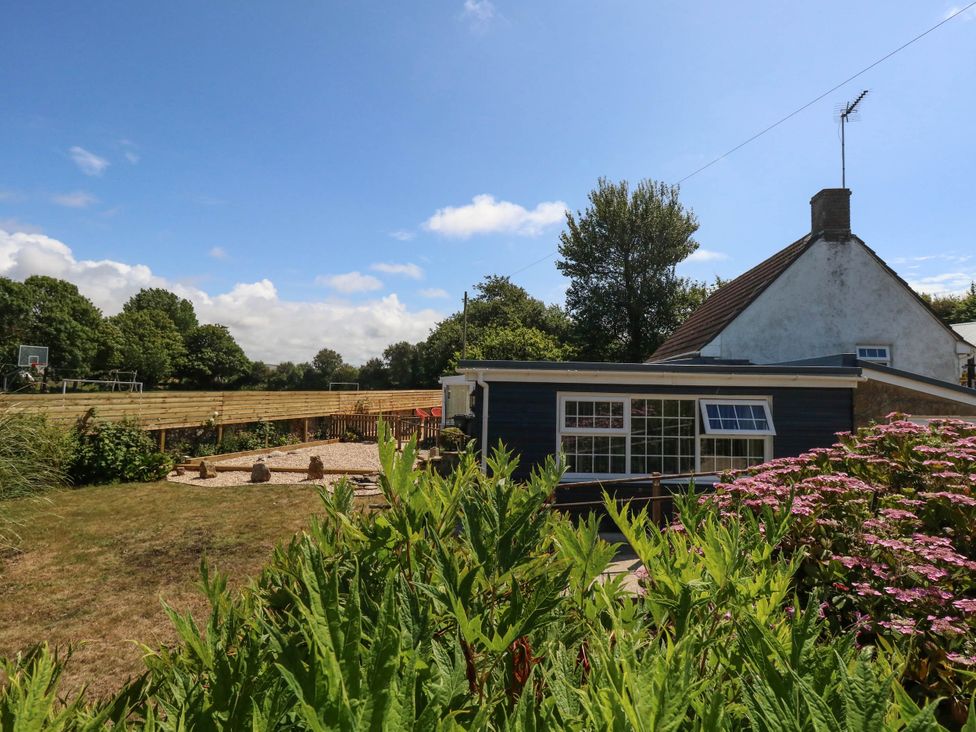 A garden with a house and basketball court at Greenwich Cottage in Burton Bradstock