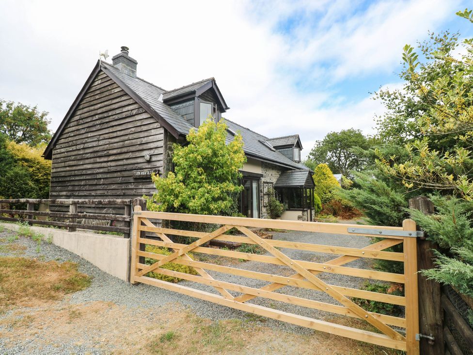 A house with a wooden gate and surrounding trees at Penrhiwoli Barn Cefn Gorwydd
