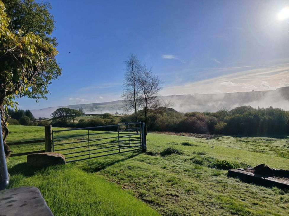 A view of a grassy area with a gate and trees at Penrhiwoli Barn in Cefn Gorwydd