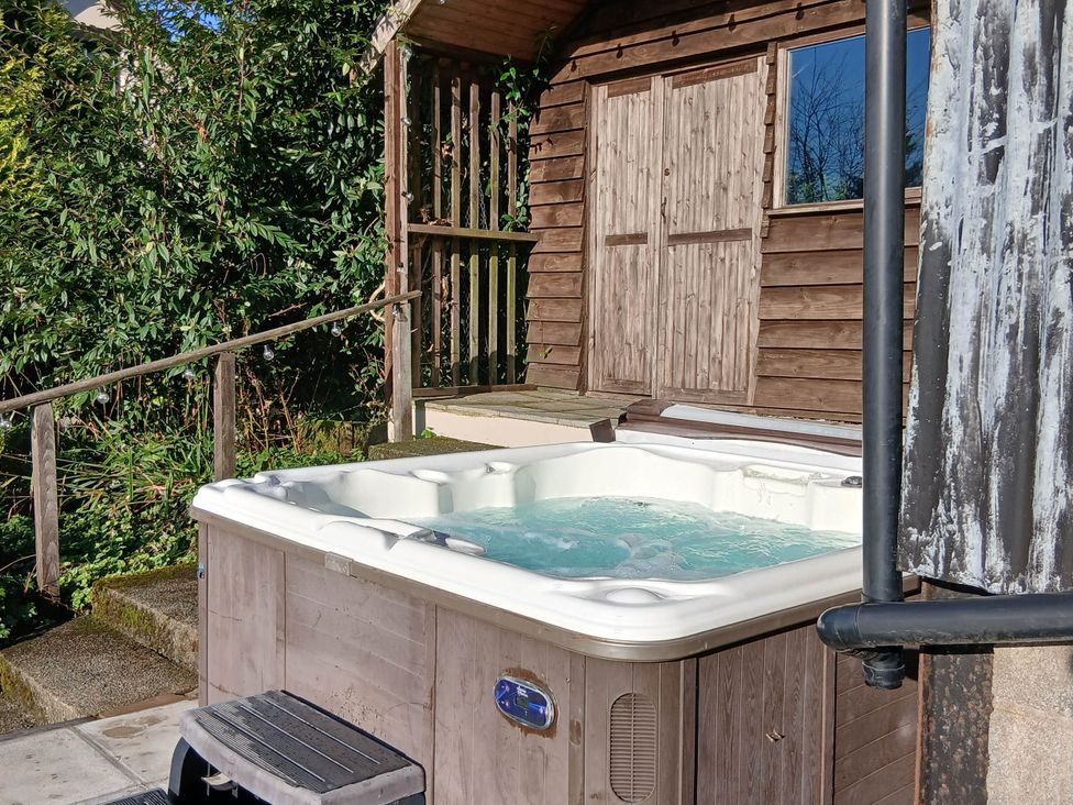 A hot tub next to a wooden cabin in an outdoor area at Penrhiwoli Barn Cefn Gorwydd