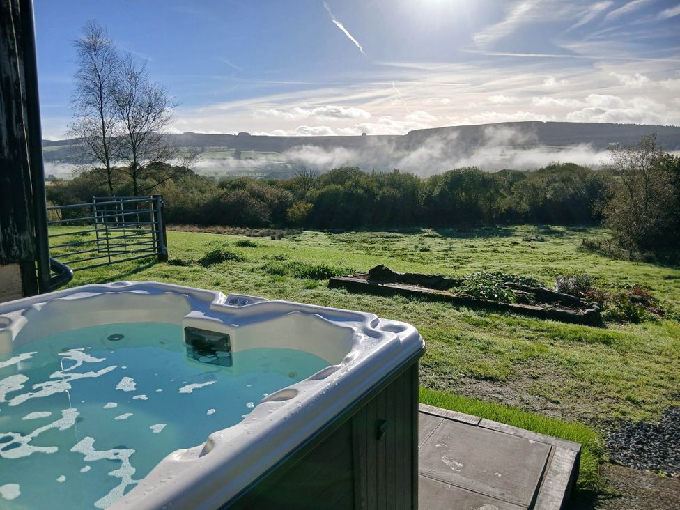 A hot tub with a view of mountains and trees at Penrhiwoli Barn in Cefn Gorwydd