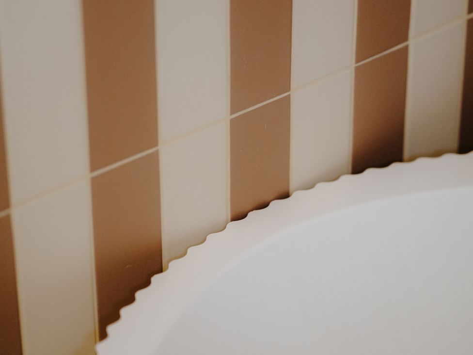 A bathtub next to striped wall tiles at Baldslow Barn in Battle near Hastings