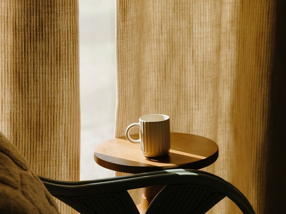 A cup on a side table with curtains in a room at Baldslow Barn in Battle near Hastings
