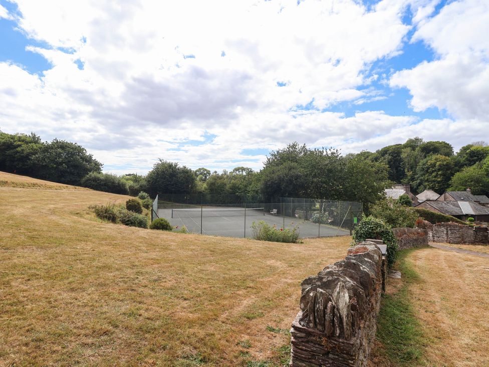 A tennis court surrounded by grass and trees at Iris at Stancombe Manor Sherford near Chillington