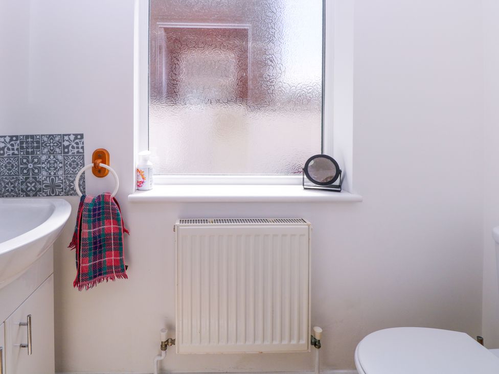 A bathroom with a sink, toilet, towel, radiator, and window at 33 North Denes in Great Yarmouth