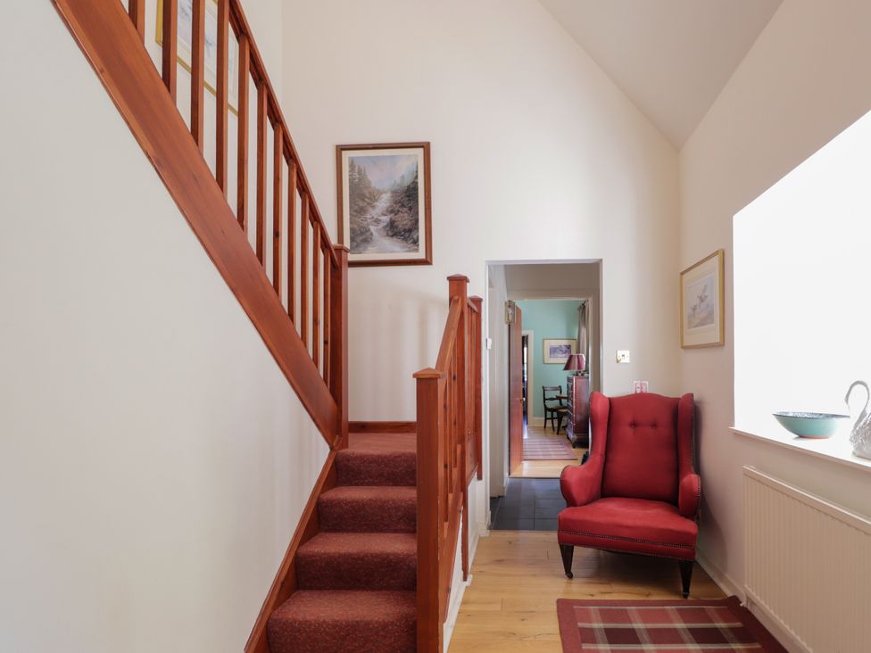 A hallway with staircase and red armchair at Tressady Coach House in Rogart