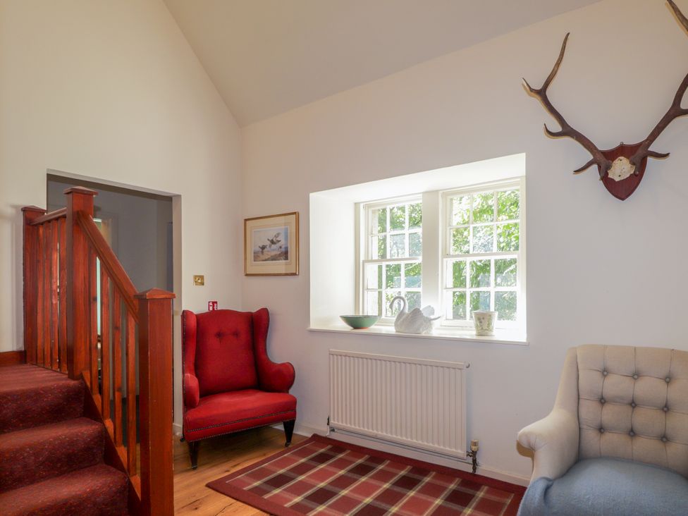 A living room with a red and cream armchair at Tressady Coach House in Rogart