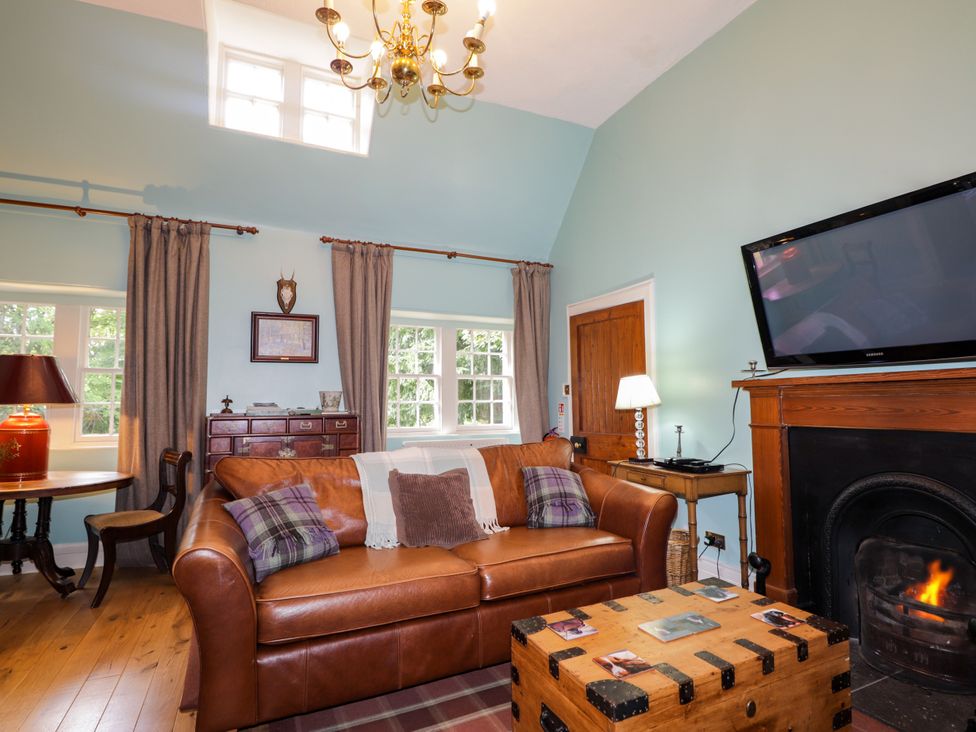 A living room with a sofa a table and a fireplace at Tressady Coach House Rogart