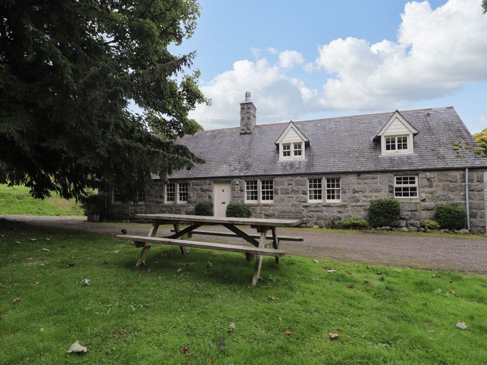 A stone building with a table and benches in front at Tressady Coach House in Rogart