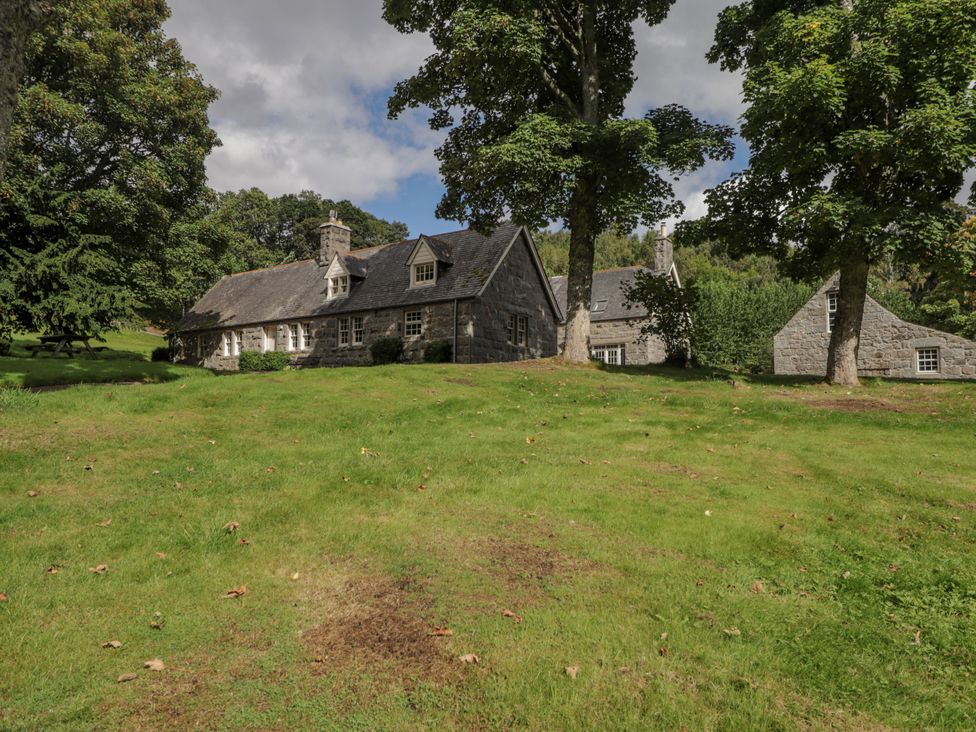 An outdoor view of a stone house and surrounding trees at Tressady Coach House in Rogart
