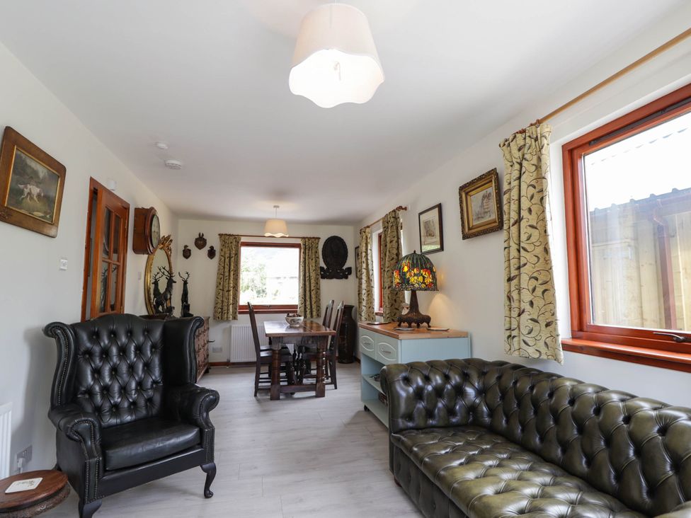 A living room with a sofa, armchair, and dining table at Park House Cannich Holiday Retreat in Cannich