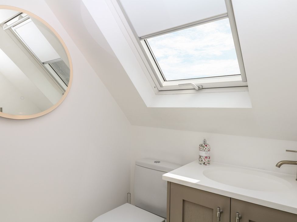 A bathroom featuring a toilet, sink, and a round mirror at Tower View Cottage in Lympstone